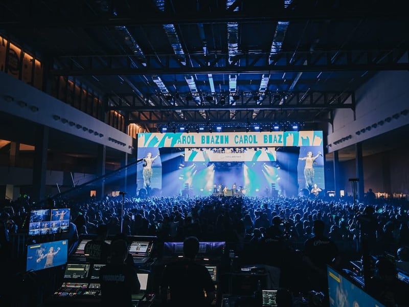 Palco da segunda edição do Meli Music visto do meio do público, com iluminação em tons de azul e verde