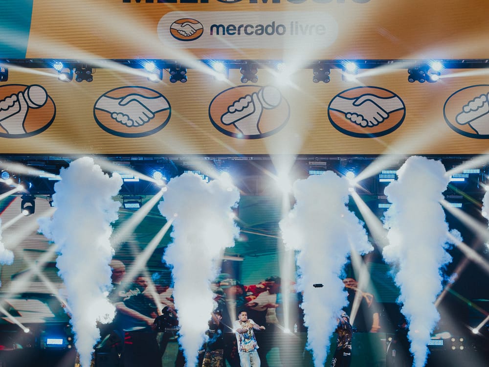Palco do Meli Music com jatos de fumaça e luzes, sob o letreiro do Mercado Livre